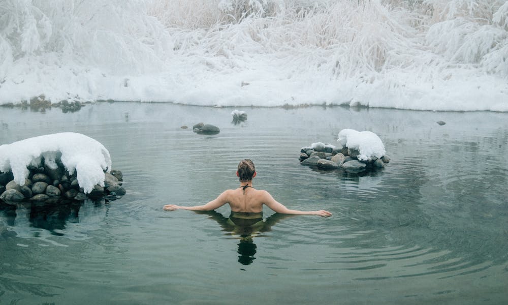 A young woman enjoying a swim in a tranquil winter lake surrounded by snow. .pexels