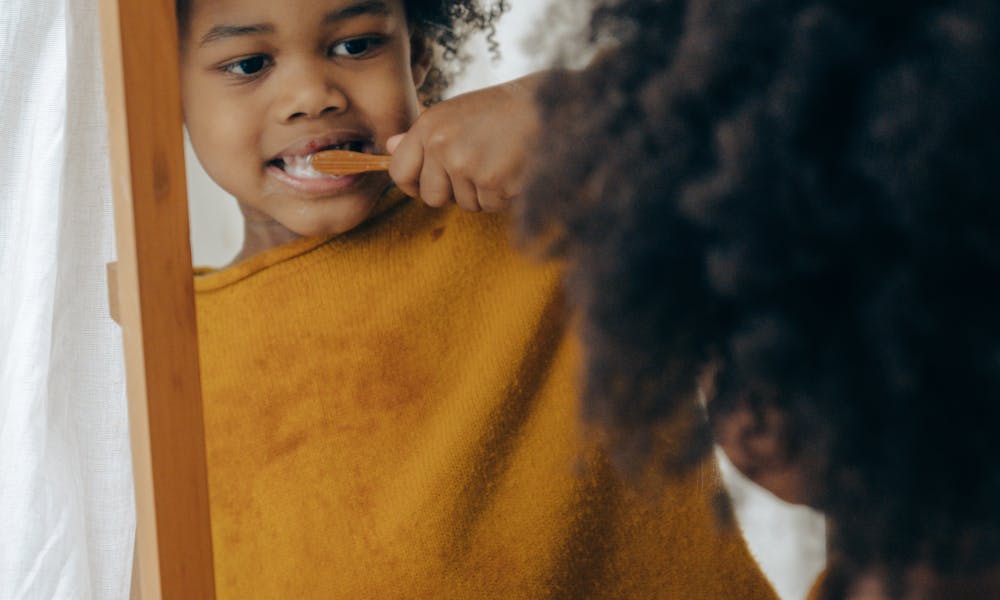 Adorable child brushing teeth with orange toothbrush in front of mirror, promoting dental care routine. .pexels