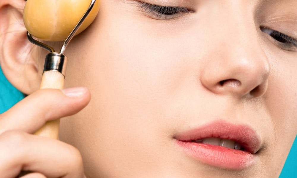 Close-up of a woman applying a jade roller for facial skin care treatment. .pexels