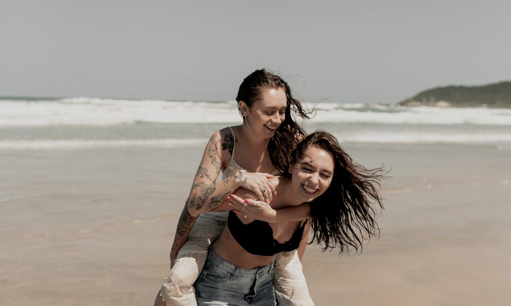 Two women enjoying a playful piggyback ride on a sunny beach day. .pexels