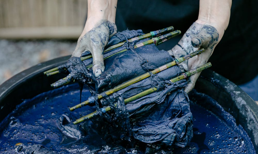 Artisan dyeing fabric using shibori technique with blue dye outdoors. .pexels