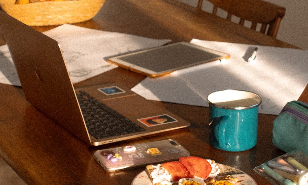 Sunlit wooden table with laptop, notebook, and breakfast, creating a cozy home workspace. .pexels