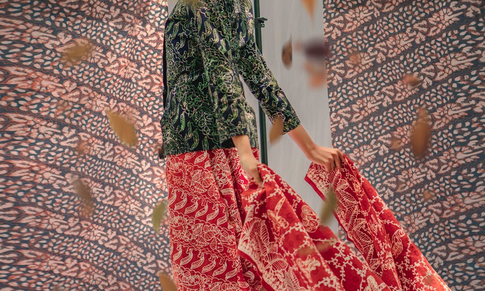 Portrait of a stylish woman in traditional Indonesian batik, with falling leaves and textile backdrop. .pexels