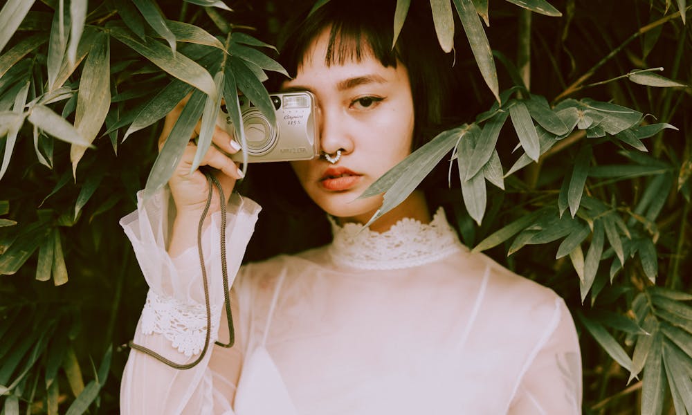 A styled portrait of a young woman hidden among lush plants capturing a vintage feel. .pexels