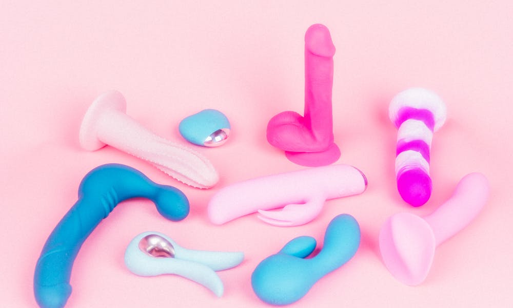 A variety of vibrators and sex toys in bright colors on a pink backdrop. .pexels