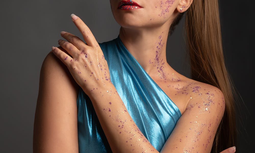 Portrait of a stylish woman with glitter makeup and blue dress, exuding confidence. .pexels