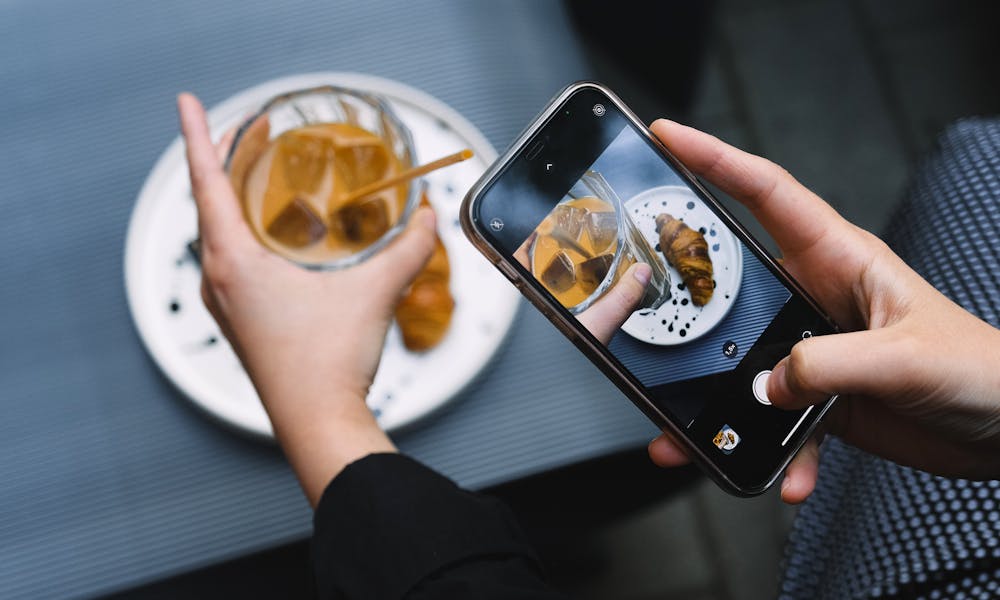 Hands taking a photo of iced coffee and croissant with a smartphone, perfect for food bloggers. .pexels