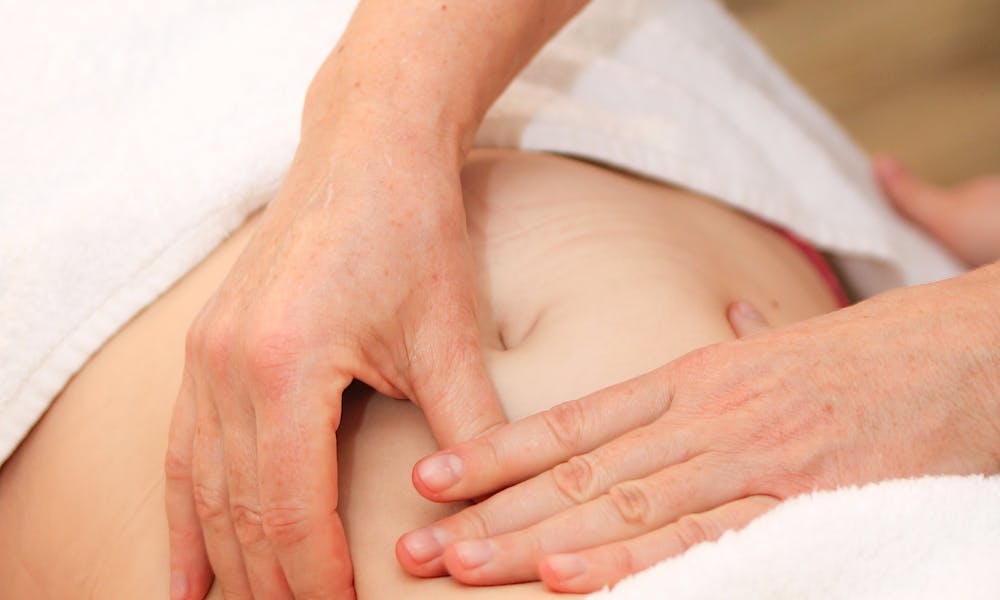 Close-up of a therapist's hands performing abdominal massage therapy on a relaxed client indoors. .pexels