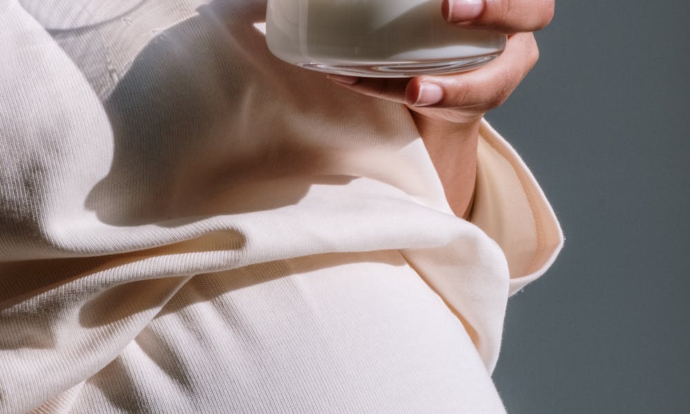 Close-up of a pregnant woman holding a glass of milk, symbolizing nurturing care. .pexels