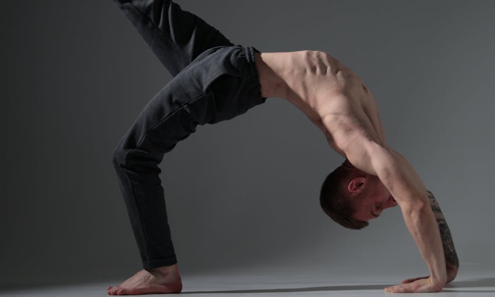 A fit man executes a yoga pose in a dimly lit studio, showcasing strength and balance. .pexels