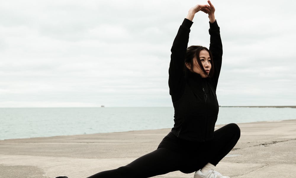 Woman performing a stretching exercise by the lake outdoors in cold weather. .pexels