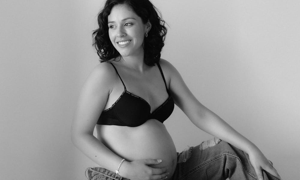 A joyful pregnant woman in black bra and jeans, sitting serenely. Captured indoors. .pexels