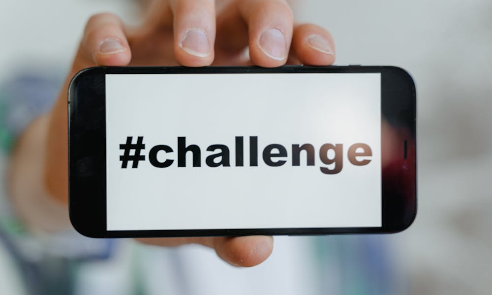 Close-up of a hand holding a smartphone displaying a '#challenge' hashtag. .pexels