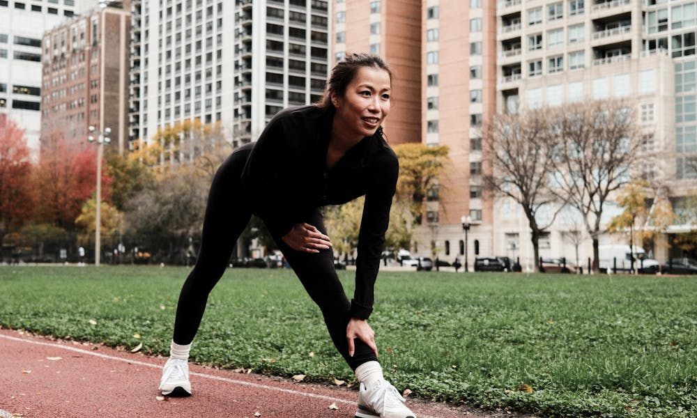 Asian woman stretching on a running track in urban Chicago with city skyscrapers in the background. Fitness and workout concept. .pexels