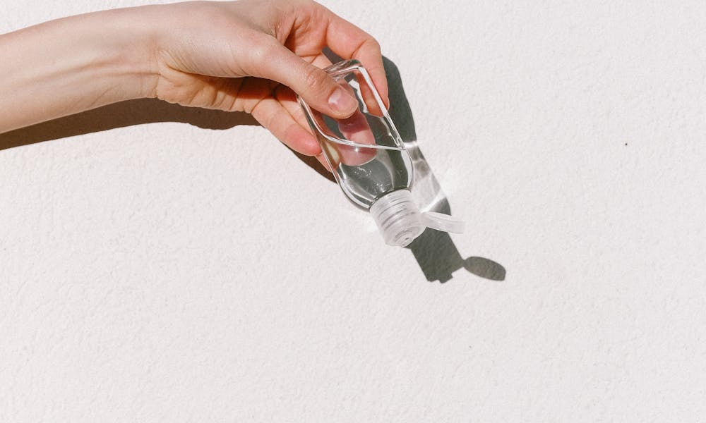 Person applying hand sanitizer against white backdrop, emphasizing hygiene and protection. .pexels