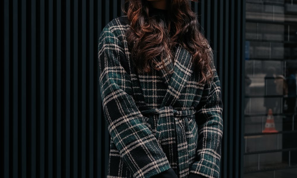 Stylish young woman posing in a checkered coat and red beret on a city sidewalk. .pexels