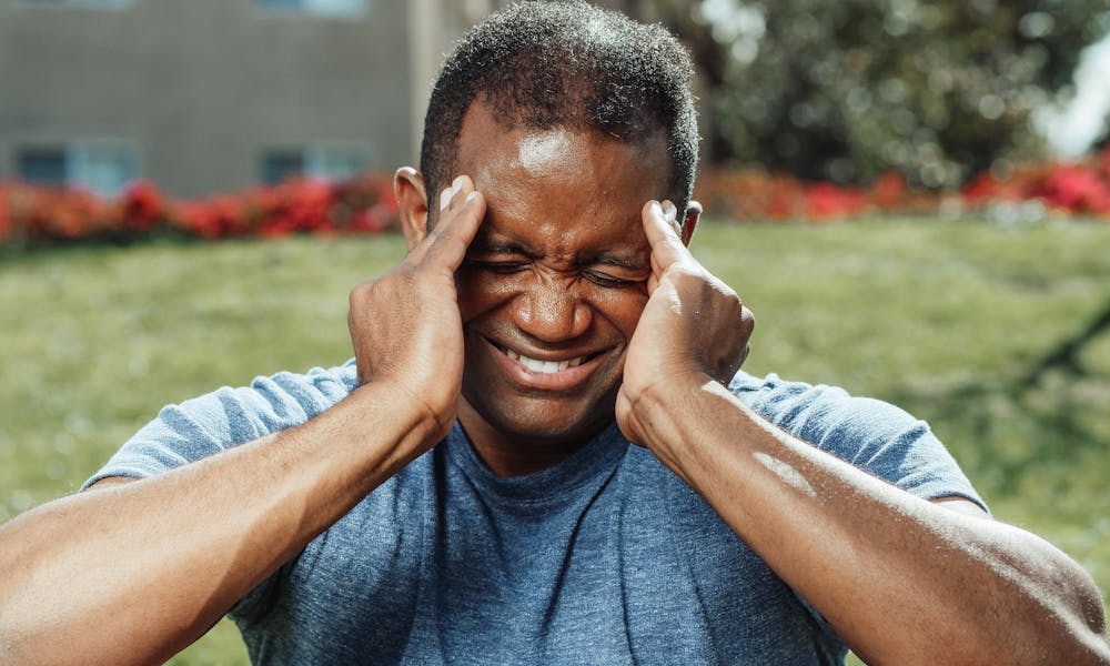 African American man massaging his temples outdoors, showing stress and emotion. .pexels