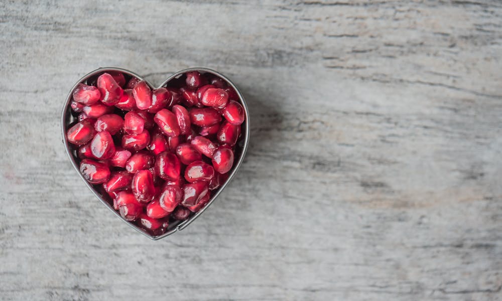 Delicious and juicy pomegranate seeds in a heart-shaped bowl on a wooden table. .pexels