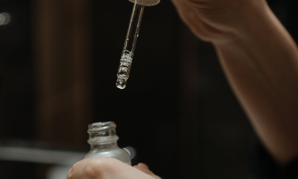 Hands holding a serum dropper applying skincare product in a bathroom setting. .pexels