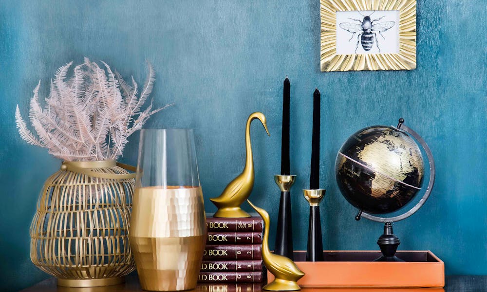 Stylish home decor arrangement including a globe, books, candles, and vases on a blue backdrop. .pexels