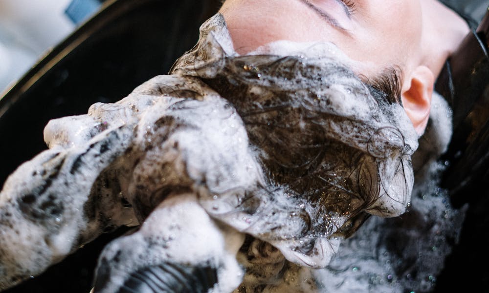 A woman getting her hair washed at a salon sink by a professional stylist wearing black gloves. .pexels