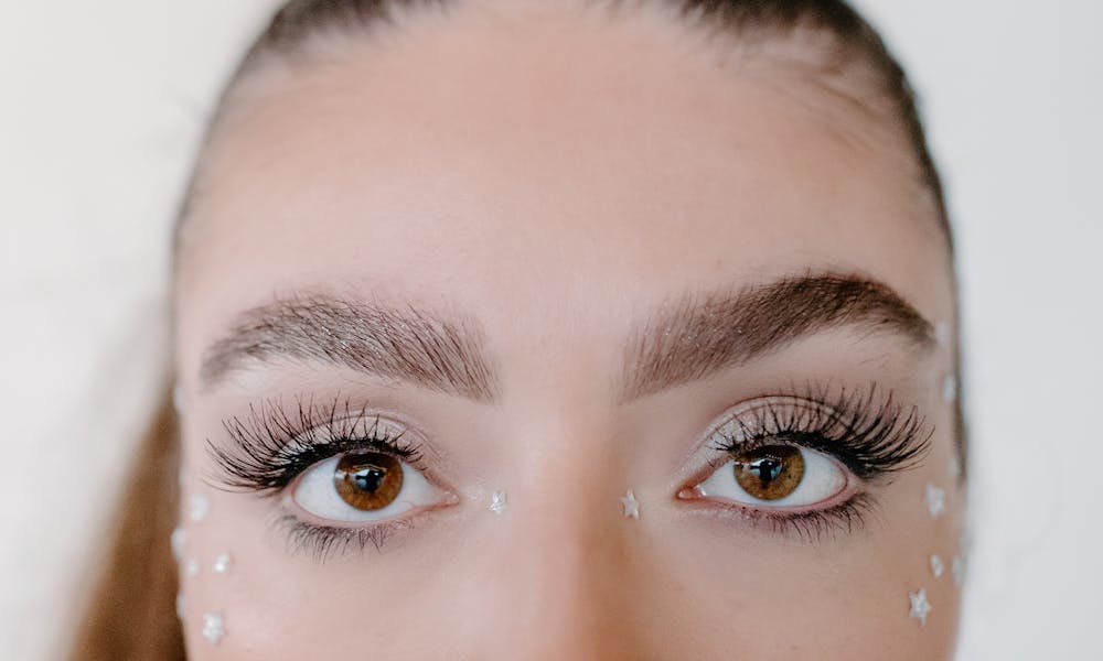 A close-up image capturing a woman's eyes adorned with decorative star art and makeup. .pexels