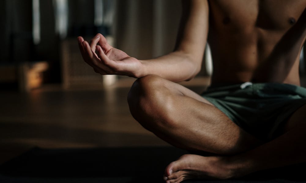 A shirtless man in a yoga studio meditating in the lotus position for relaxation and wellness. .pexels