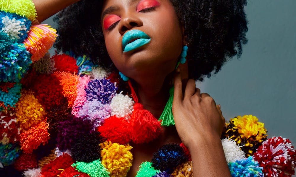 Striking portrait of a woman wearing a colorful pom pom jacket with bold makeup. .pexels