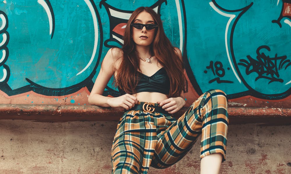 Trendy woman in plaid pants poses confidently against vibrant graffiti wall. .pexels