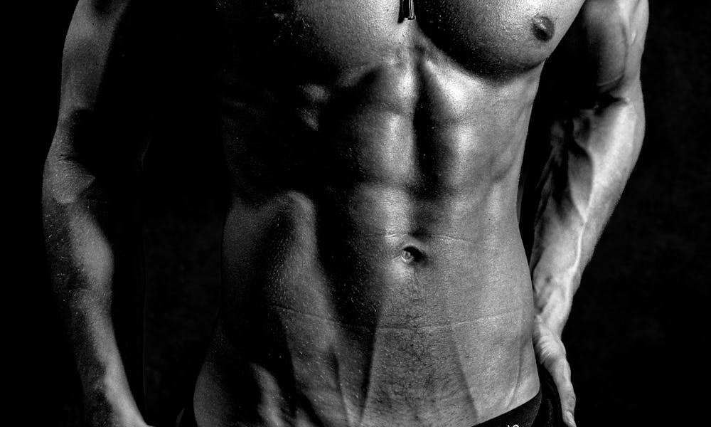 Striking black and white image of a shirtless muscular male model posing confidently. .pexels