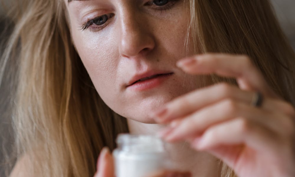 A young woman applying moisturizing cream indoors, focusing on her skincare routine. .pexels