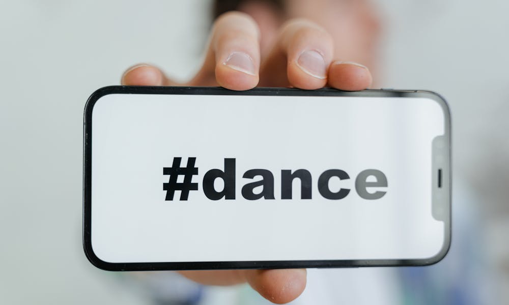 Close-up of a phone screen displaying the #dance hashtag, held by an adult. .pexels