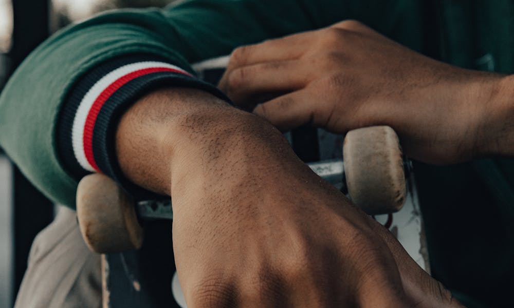 A skateboarder rests his hand over a skateboard outdoors, capturing urban street style. .pexels