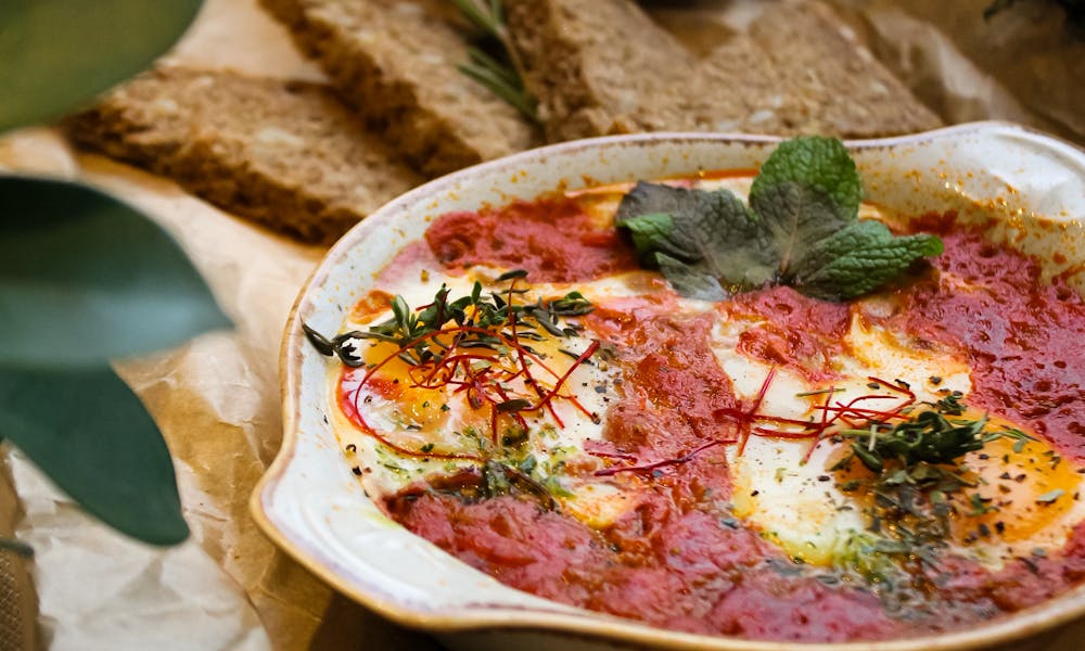 Savory shakshuka served with rustic bread on a wooden table setting. .pexels