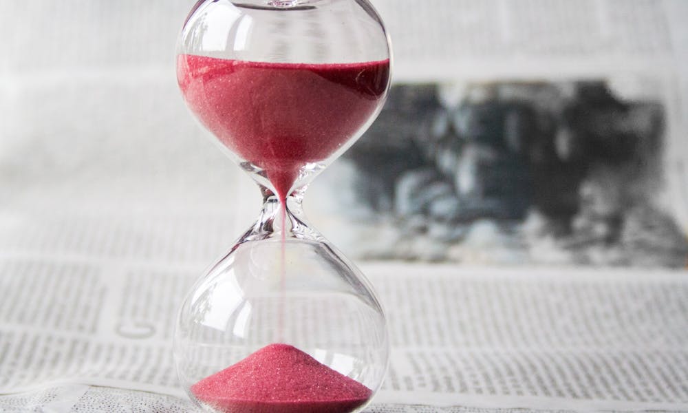 Close-up of a transparent hourglass with pink sand flowing, placed on a newspaper background. .pexels