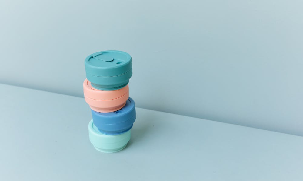 Minimalist image of stacked reusable cup lids in pastel colors on a plain blue surface. .pexels