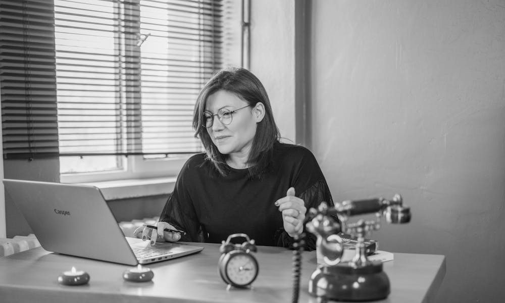 A businesswoman using a laptop at her desk with a vintage phone and an alarm clock, creating a mix of modern and retro vibes. .pexels