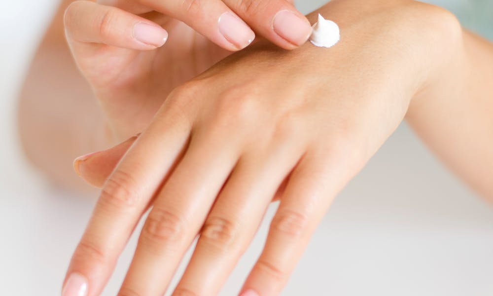 A woman applying cream on her hands, highlighting skincare and self-care concepts. .pexels