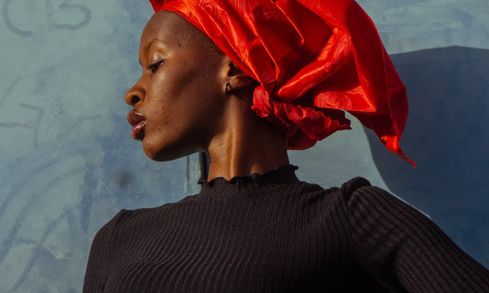 Stylish portrait of a woman wearing a vibrant red headwrap against a blue background. .pexels