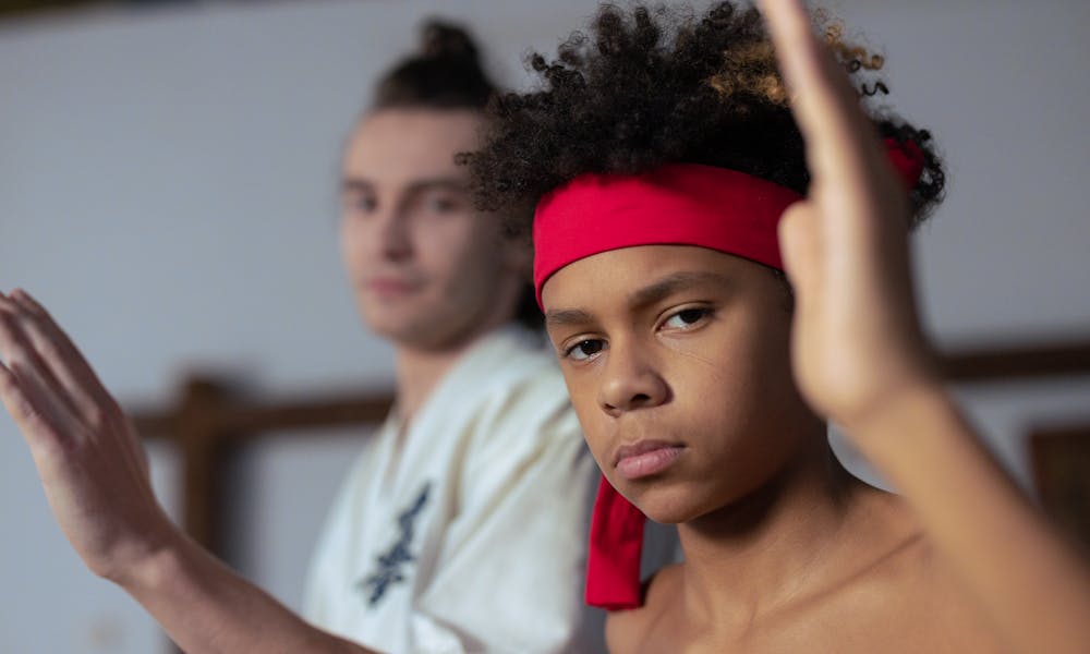 Two boys practicing martial arts indoors, with focus on the black boy in a red headband. .pexels