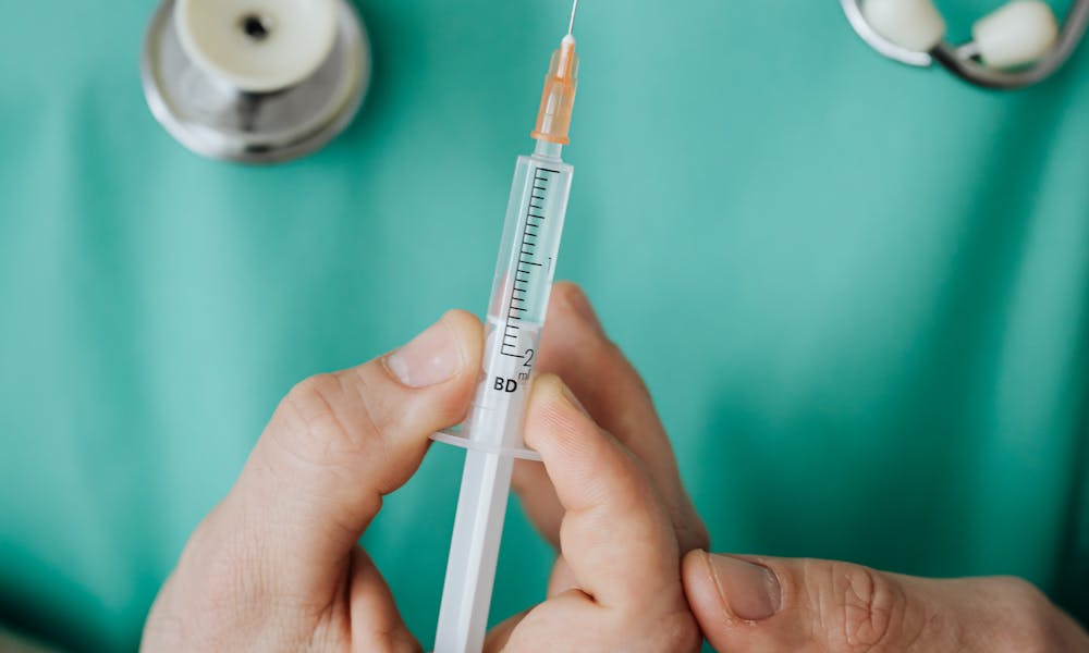 Doctor holding a syringe, ready for injection, with stethoscope. .pexels