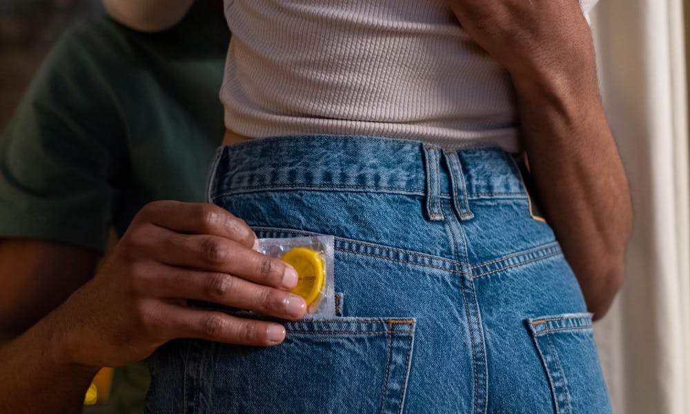 A couple embraces intimately, promoting safe sex with a condom in the pocket. .pexels