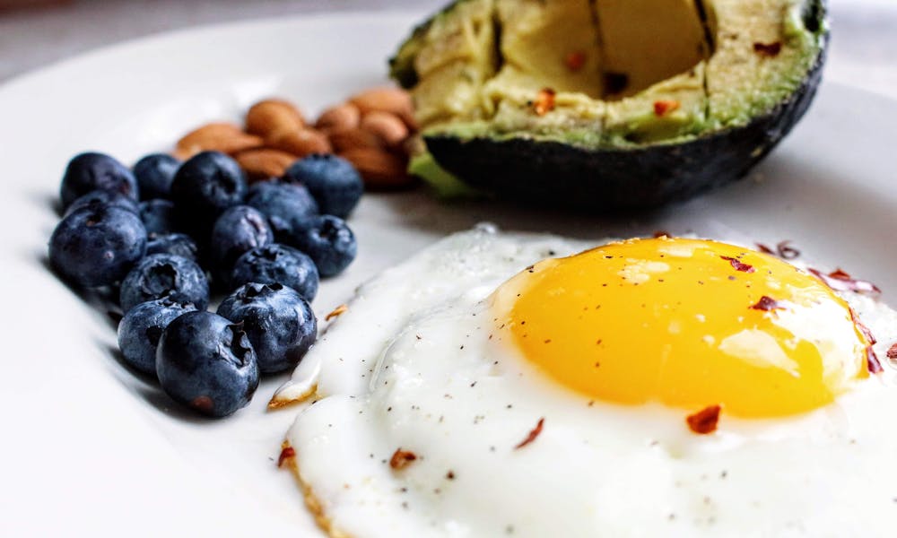 A nutritious breakfast featuring a fried egg, avocado, blueberries, and almonds. .pexels