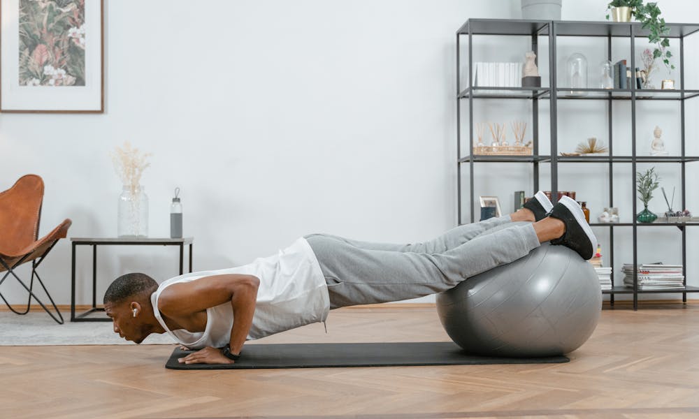 Adult doing push-ups with an exercise ball indoors for fitness and health. .pexels