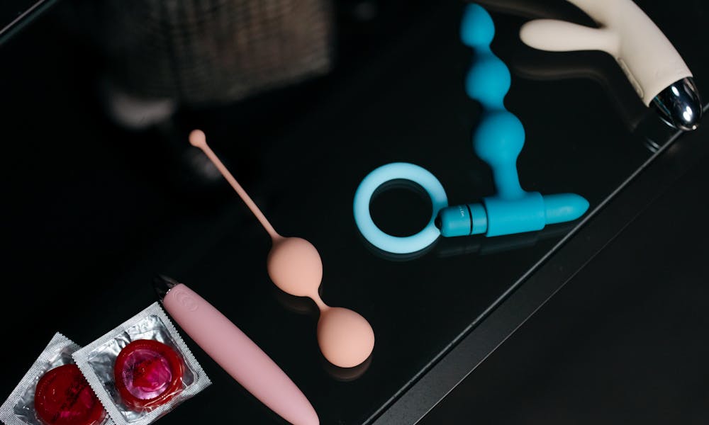 A collection of various sex toys and condoms on a reflective tabletop for safe and sensual pleasure. .pexels