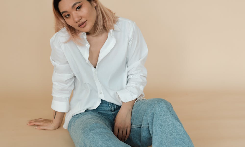 A young woman in denim jeans and white blouse sitting on the floor, exuding a stylish and casual vibe. .pexels