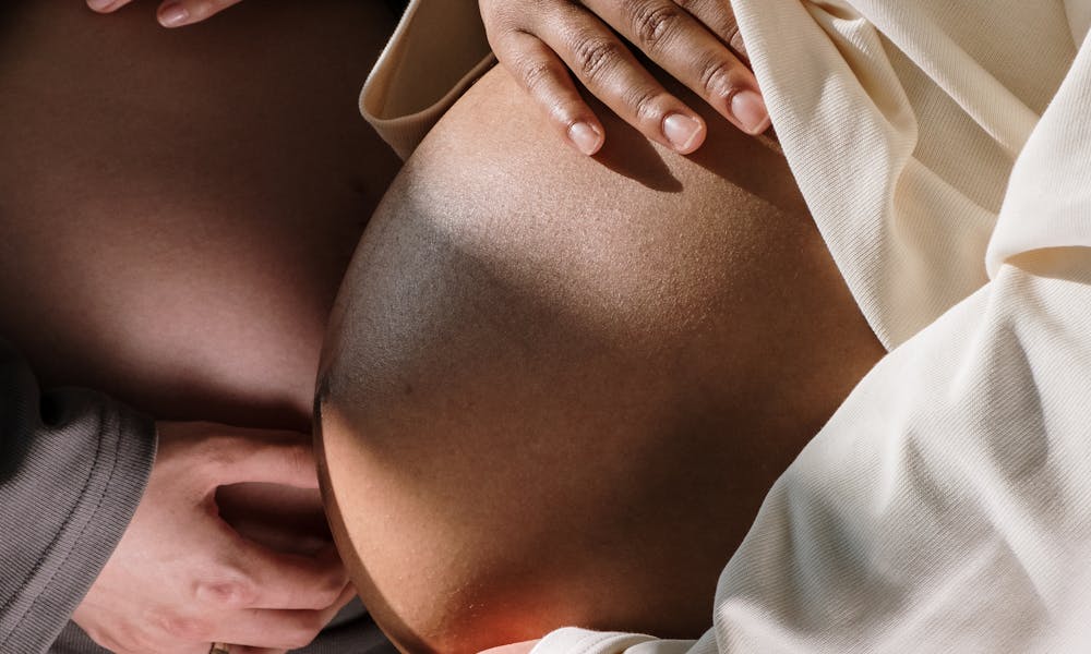 A close-up view showing two pregnant women embracing their baby bumps. .pexels