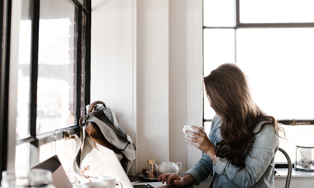 A young woman working on her laptop, sipping coffee in a bright café setting. .pexels