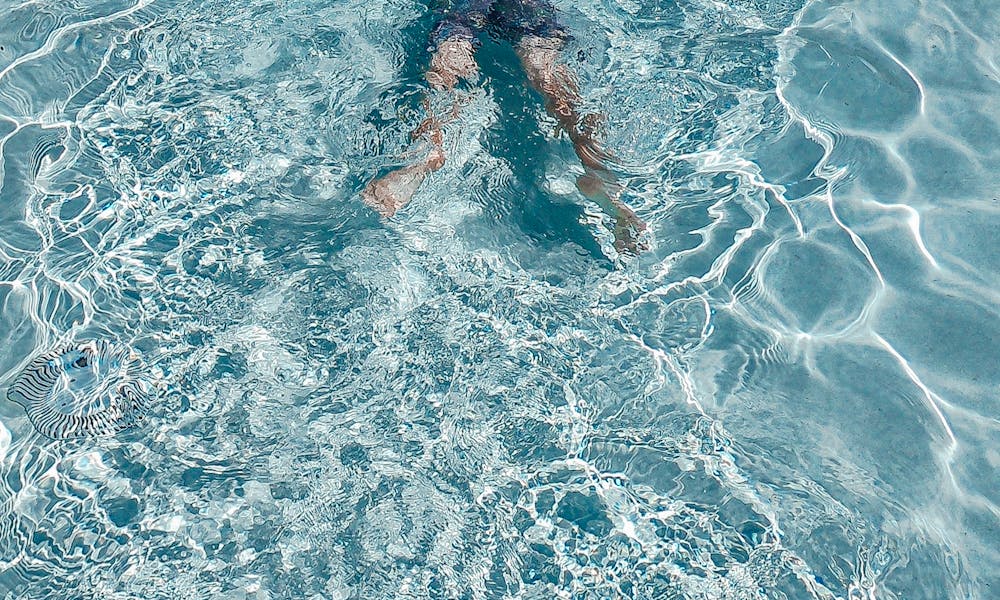 Man enjoying a relaxing swim in a crystal-clear outdoor pool. .pexels