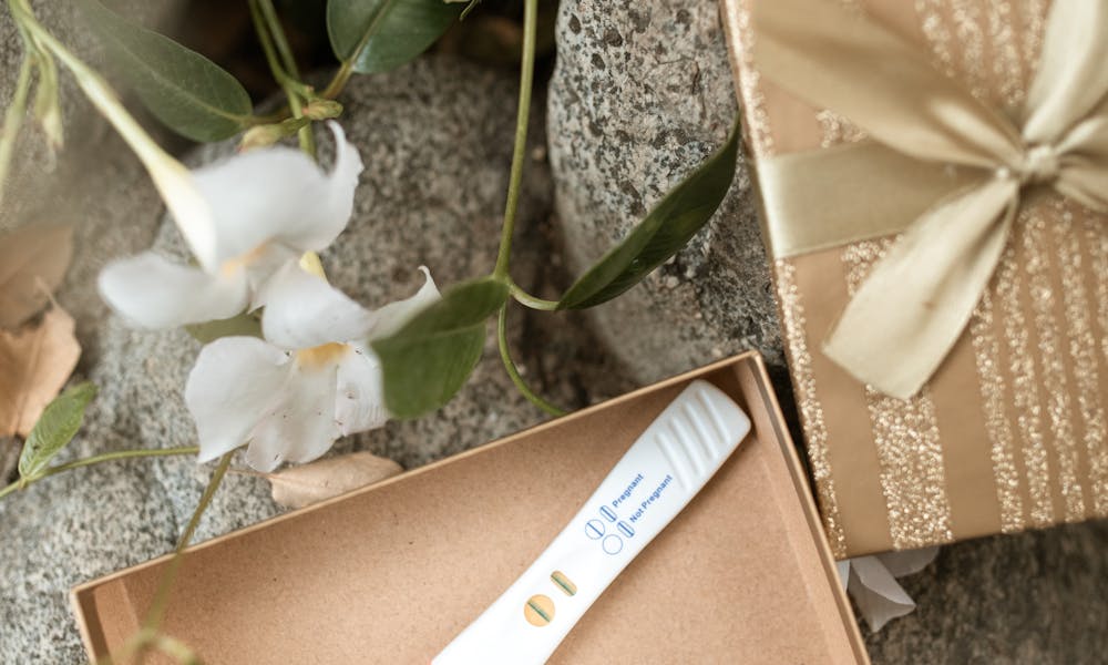 Positive pregnancy test displayed in a decorative gift box with flowers. .pexels